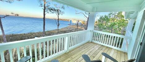 A covered porch with a view of the water, white railings, and two Adirondack chairs.