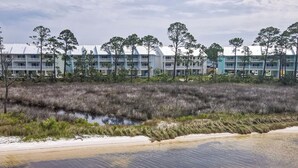 A coastal hotel with multiple-story buildings, a beachfront, and a marshy area with trees.