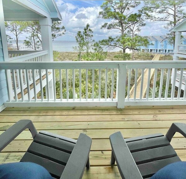 A wooden deck with two lounge chairs facing a white railing overlooking a beach and ocean.