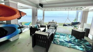 Een overdekt terras met uitzicht op zee, een surfboard en een hangmat.