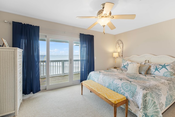 A bedroom with a bed, a bench, a ceiling fan, a nightstand, and a view of the ocean.