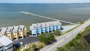 A coastal hotel with multiple-story buildings, a parking lot, and a pier extending into the water.