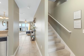 Un pasillo con una zona de cocina, una escalera y vista a un salón.