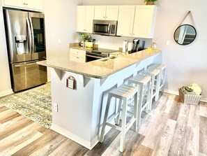 A kitchen with a central island, bar stools, a refrigerator, a microwave, and a sink.