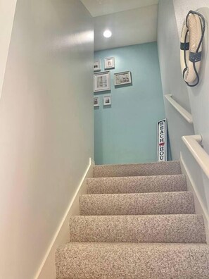 A staircase with a light blue wall at the top, a sign reading 'BEACH HOUSE,' and a wall-mounted telephone.