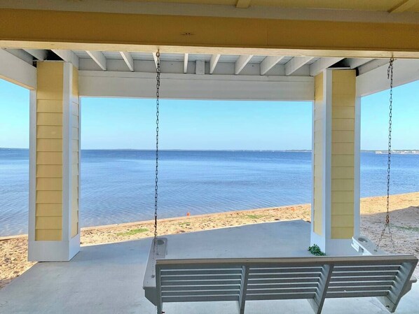 A covered outdoor area with a swing, overlooking a beach and the sea.