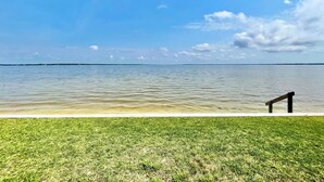 A grassy area with a wooden bench by a calm body of water under a clear sky.