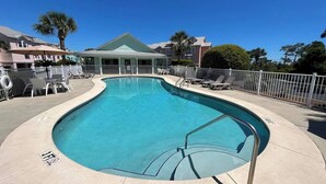 A swimming pool with a curved edge, surrounded by lounge chairs and a white fence.