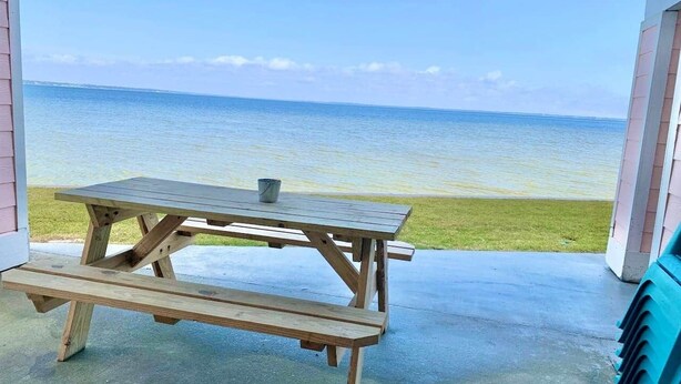 A wooden picnic table with benches, a metal cup, and a view of the ocean.