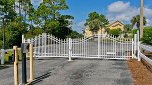 A gated driveway leading to a residential area with a yellow house and a white fence. - Paradise Point: Waterfront Unit with 2 Kayaks! (Pensacola)