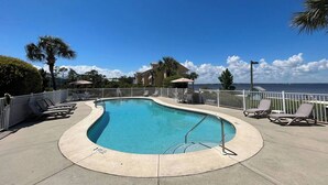 A pool area with a curved pool, lounge chairs, and a view of the ocean. - Serenita Ora: Quiet Waterfront Unit with 2 Kayaks! (Pensacola)