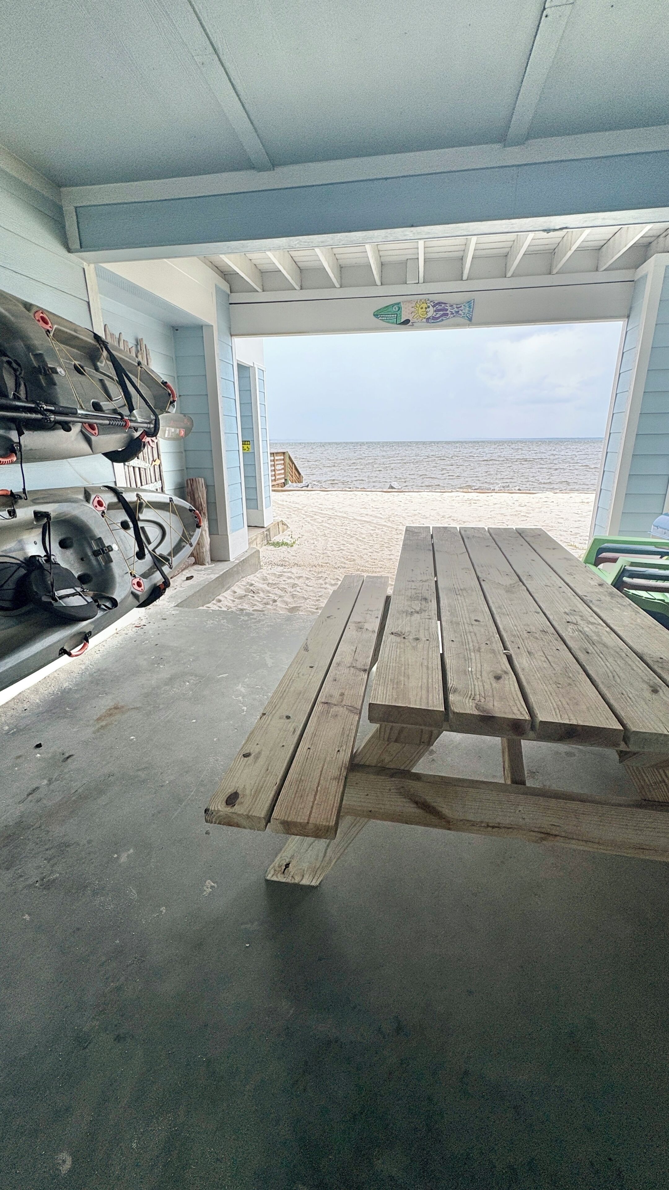 A covered outdoor area with a picnic table, a kayak, and a surfboard rack.