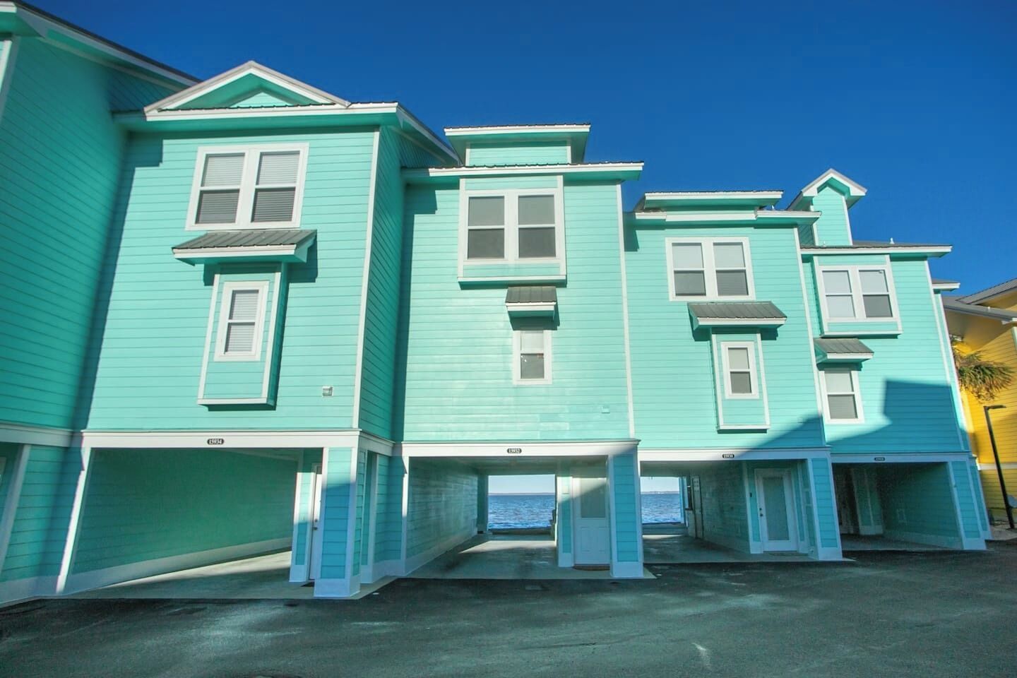A row of turquoise houses with white trim, a clear blue sky, and a view of the ocean.