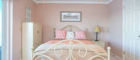 A bedroom with a bed, a nightstand, a lamp, a wardrobe, and a wall with a sign.