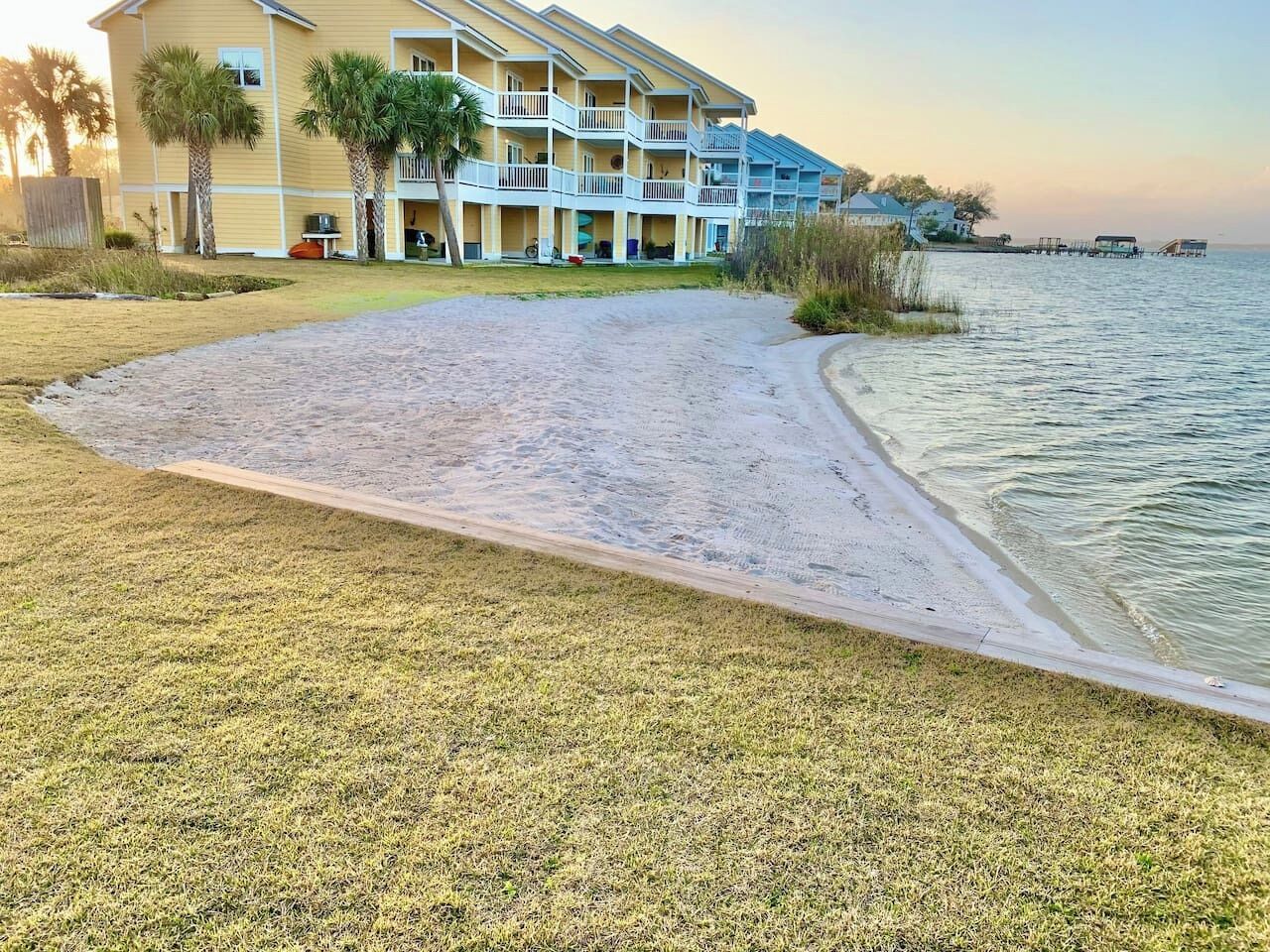 A beachfront hotel with a paved walkway leading to the beach, palm trees, and a view of the ocean.