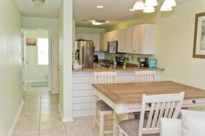 Une cuisine avec des meubles blancs, un réfrigérateur en acier inoxydable, une table à manger en bois et une vue sur la salle de bain.