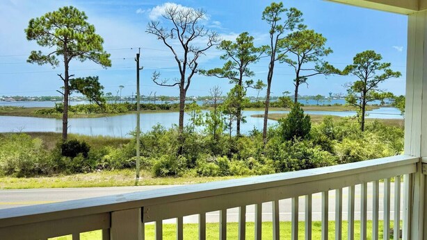 A view from a porch overlooking a lake with trees and a grassy area.