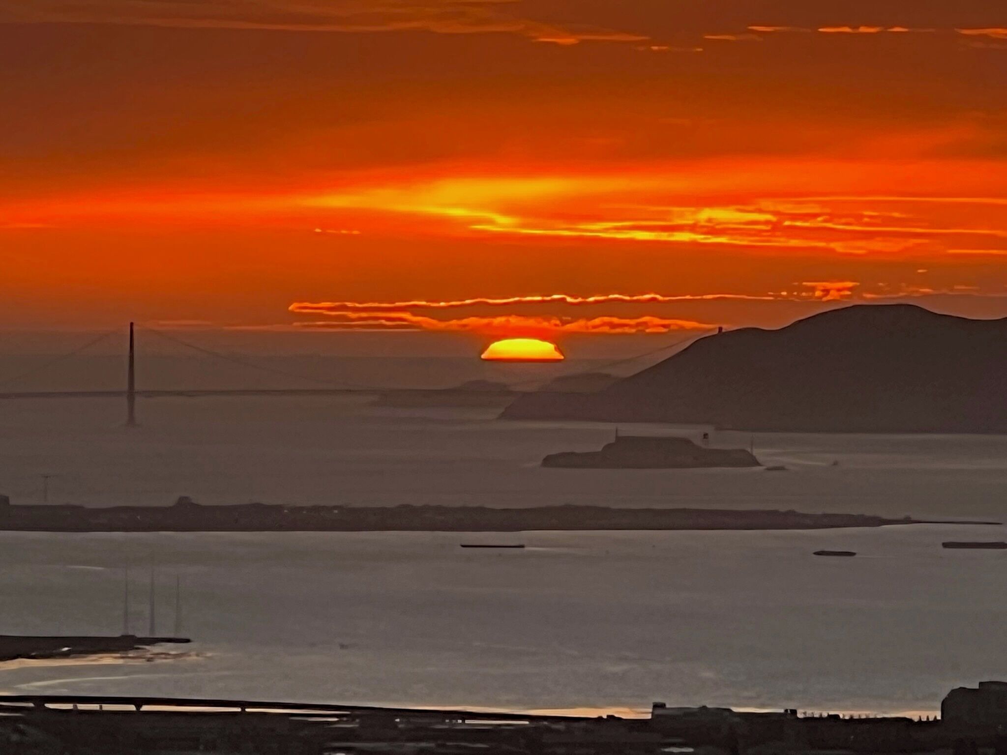 Un coucher de soleil sur une étendue d'eau, avec un pont en arrière-plan.