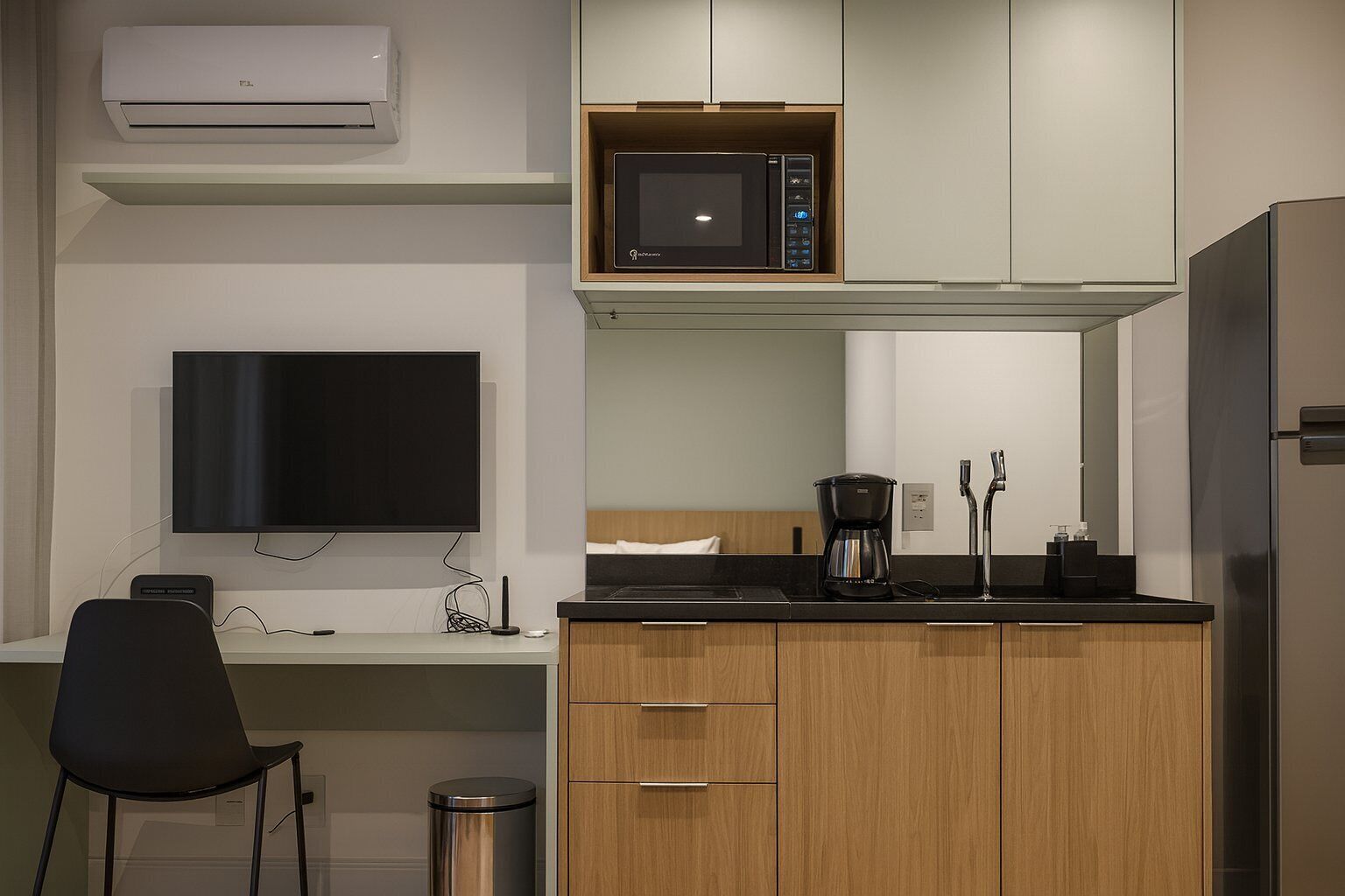 Cocina compacta con microondas, cafetera y televisor montado en la pared.