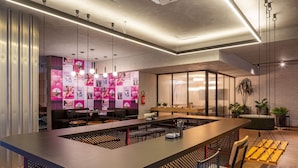 Zona de bar moderna con una barra larga, asientos y una pared decorativa con carteles.