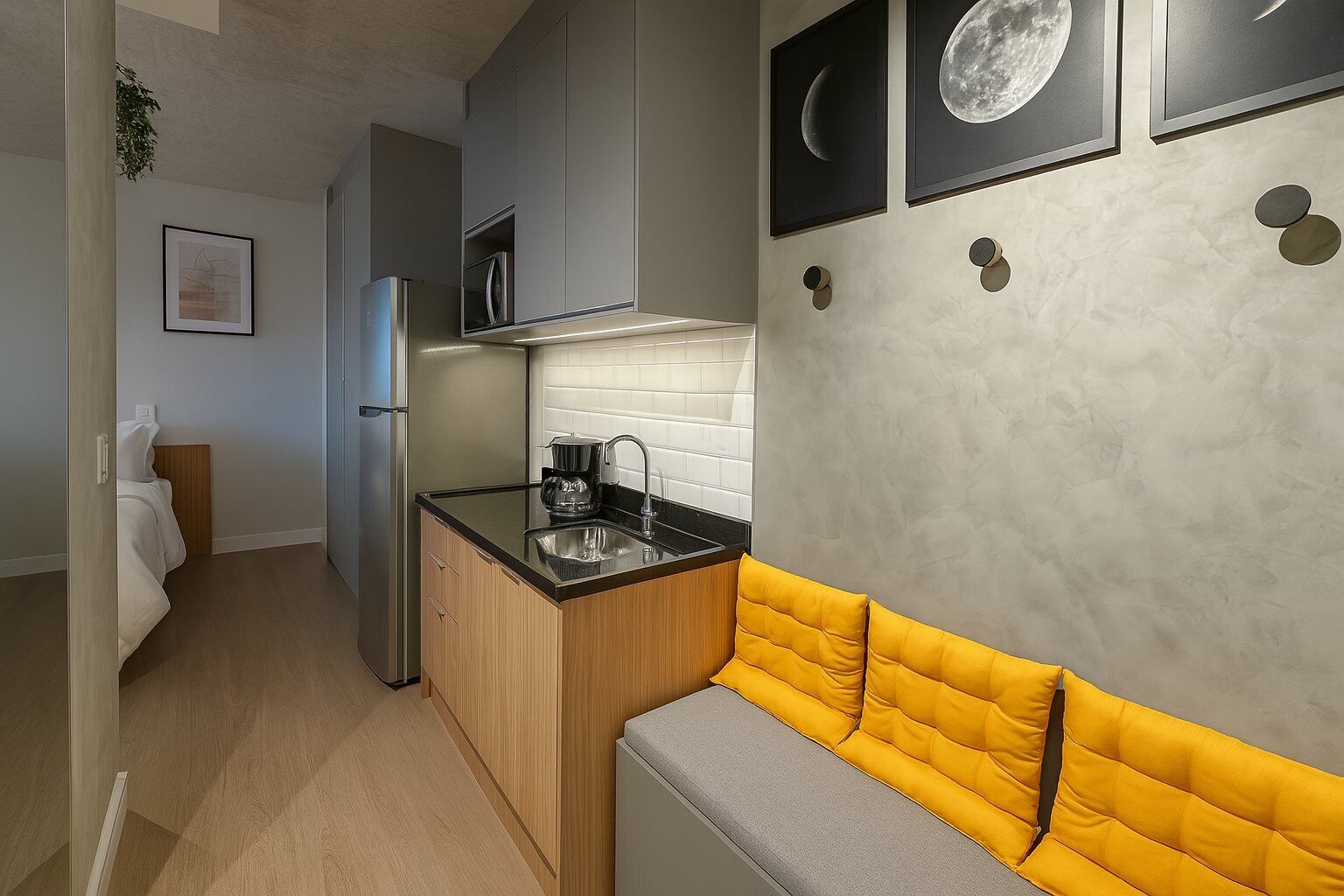 Une cuisine compacte équipée d’un four à micro-ondes encastré, d’une machine à café et d’un évier. Contre le mur, on trouve un banc jaune rembourré et, au mur, un tableau représentant la lune.