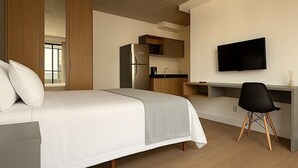 Una habitación de hotel moderna con cama, escritorio, televisión y kitchenette.