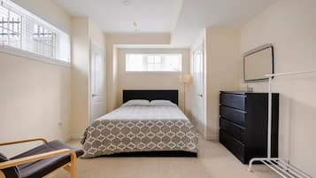 Een slaapkamer met een bed, een dressoir, een stoel en een raam met jaloezieën.