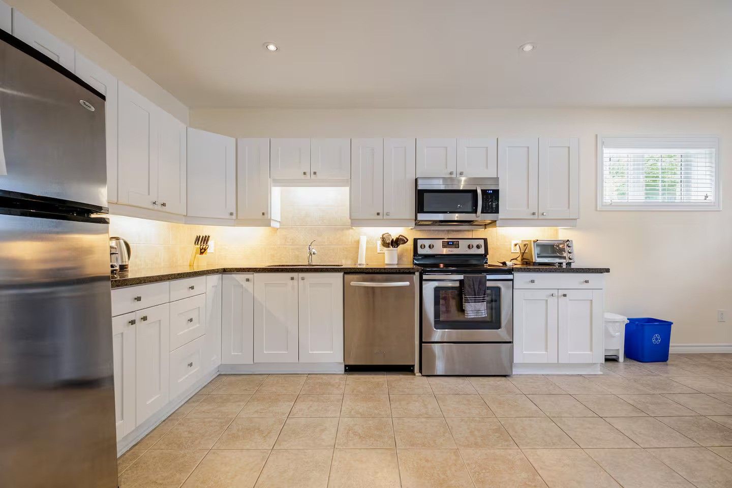 A modern kitchen with white cabinets, stainless steel appliances, and a tiled floor.