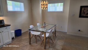 A dining area with a glass table, white chairs, a blue trash bin, and a kitchen area with a microwave. - Spacious 2 BR, 3 beds, sleeps 6, kitchen, laundry (Richmond Hill)