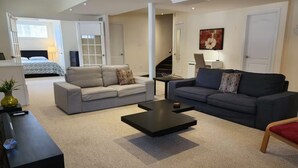 A modern living room with two sofas, a coffee table, and a TV. A staircase leads to a bedroom with a bed. - Spacious 2 BR, 3 beds, sleeps 6, kitchen, laundry (Richmond Hill)