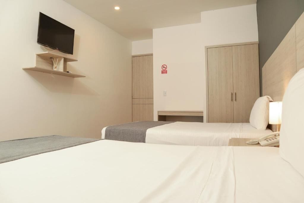 Une chambre d’hôtel avec deux lits, un téléviseur fixé au mur, une armoire et un téléphone sur la table de chevet.