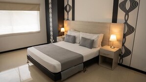 Et moderne hotelværelse med en stor seng, to sengeborde med lamper, et vindue med persienner og et mønstret vægdesign.
