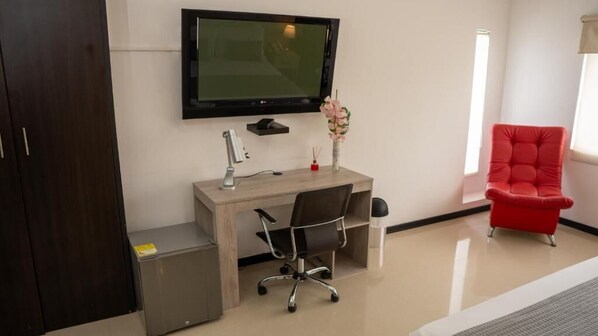 A room with a desk, chair, TV, and a red chair.