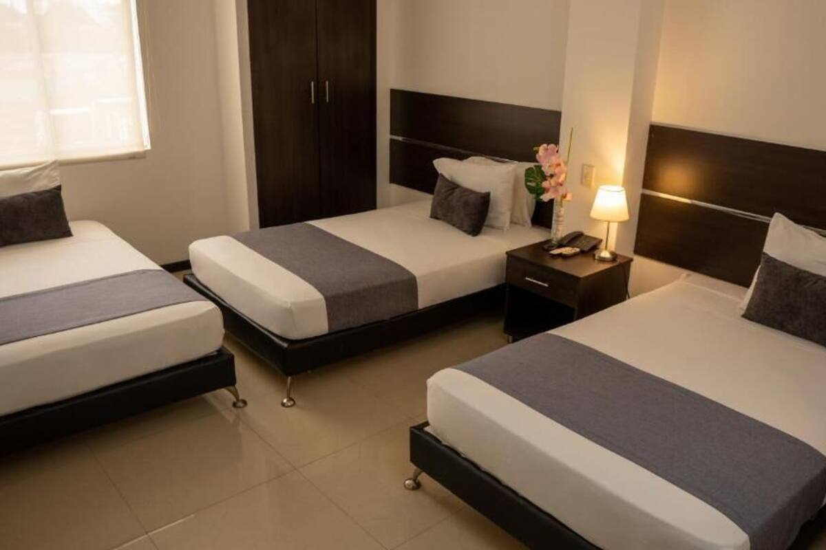 Una habitación de hotel con tres camas individuales, cada una con una mesita de noche y lámpara.