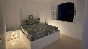 A bedroom with a bed, a window, and a hanging light fixture.