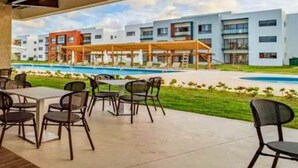 An outdoor patio area with tables and chairs, a pool, and modern buildings in the background. - Punta Cana Beach Retreat-Costa Bavaro (Punta Cana)