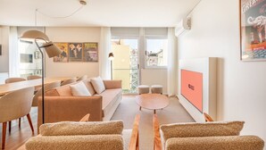 Una sala de estar moderna con un sofá, sillas, una mesa de comedor y un amplio ventanal con vistas a edificios.