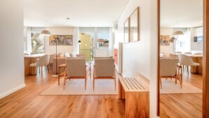 Una sala moderna con piso de madera, un sofá, una mesa de comedor con sillas y una zona de cocina al fondo.
