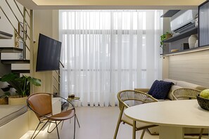A modern living room with a flat-screen TV, a dining table, and two wicker chairs.