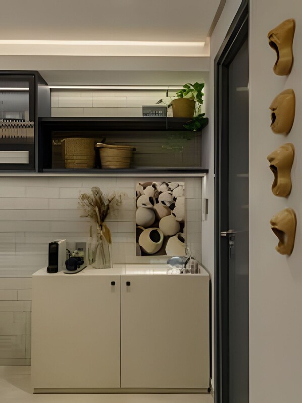 Une cuisine moderne avec des meubles blancs, un plan de travail noir et un mur décoratif orné de pots en céramique et d’une plante.