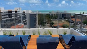 A balcony with a view of a modern building and the ocean. - Box 150 (Joao Pessoa)