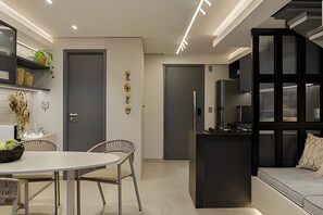 A modern living room with a sofa, a dining table with chairs, a kitchen area, and a staircase. - Box 150 (Joao Pessoa)