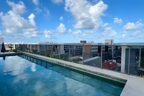 Una piscina infinita en la azotea con vistas despejadas al horizonte de la ciudad y edificios al fondo.