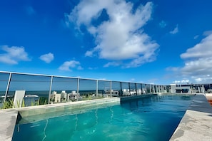 Une piscine à débordement située sur le toit, offrant une vue dégagée sur l’océan et le paysage urbain.