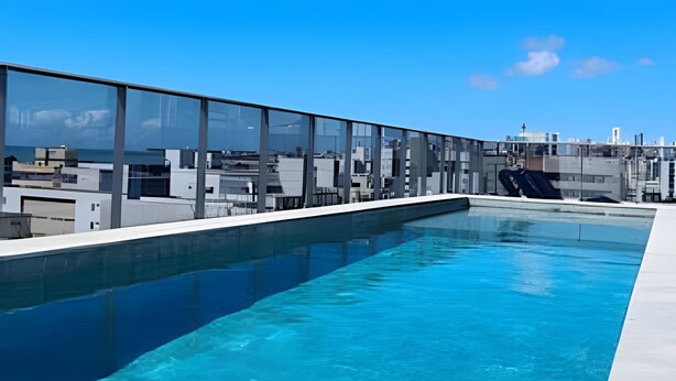 A rooftop swimming pool with clear blue water, surrounded by modern buildings and a clear sky. - Box 150 (Joao Pessoa)