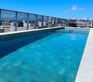 A rooftop swimming pool with clear blue water, surrounded by modern buildings and a clear sky. - Box 150 (Joao Pessoa)