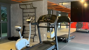 Un gimnasio con bicicletas estáticas, una cinta de correr y una máquina de ejercicios de pared.