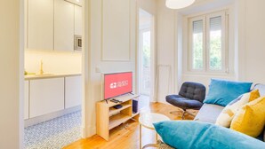 A modern living room with a sofa, a television, and a kitchen area with cabinets and a sink. - GuestReady - Relaxing place in Lisbon (Lisbon)