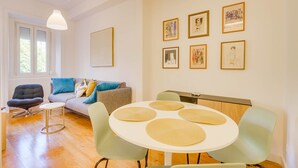 A modern living room with a sofa, a dining table with placemats, and artwork on the wall. - GuestReady - Relaxing place in Lisbon (Lisbon)