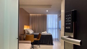 Ein modernes Hotelzimmer mit Bett, Schreibtisch, Stuhl, Sofa und einer Tür mit Zahlenschloss.